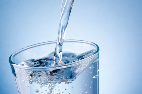 Pouring water into glass on blue background